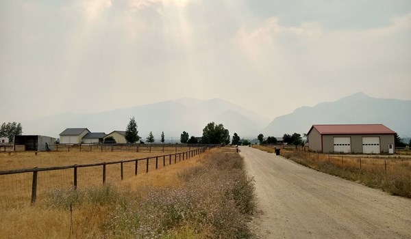 Sun poking through clouds on smoky day with view of field and mountains 