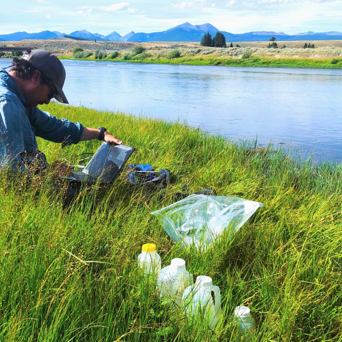 A Save Wild Trout member organizing samples by a river side in a field with mountains in the background.