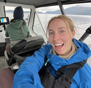 Paige Weigand smiling and sitting on a boat with a view of a lake behind her.