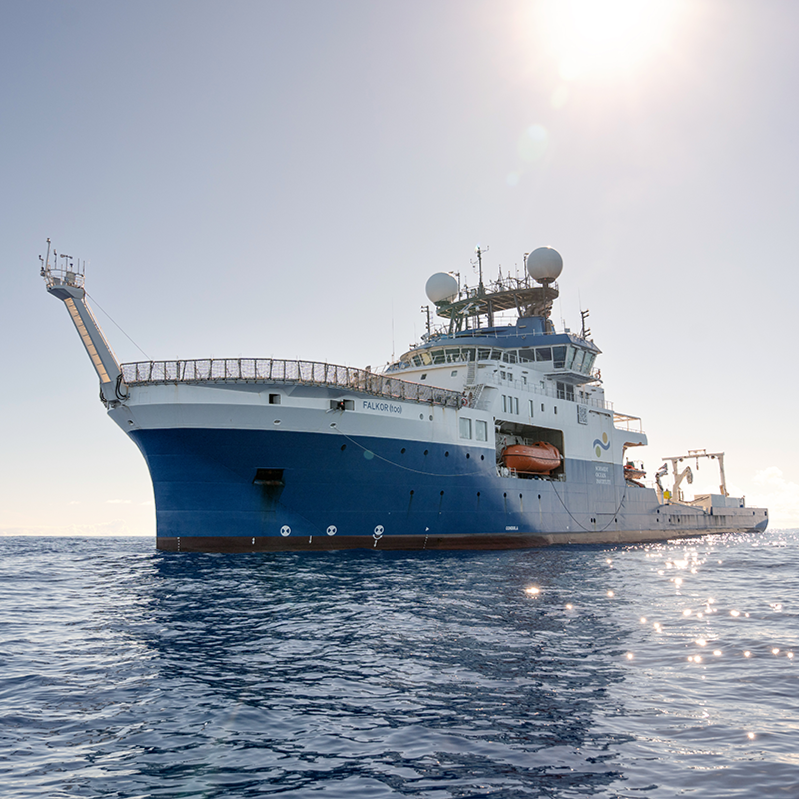 Sun shines down on large ocean research vessel over calm ocean waves