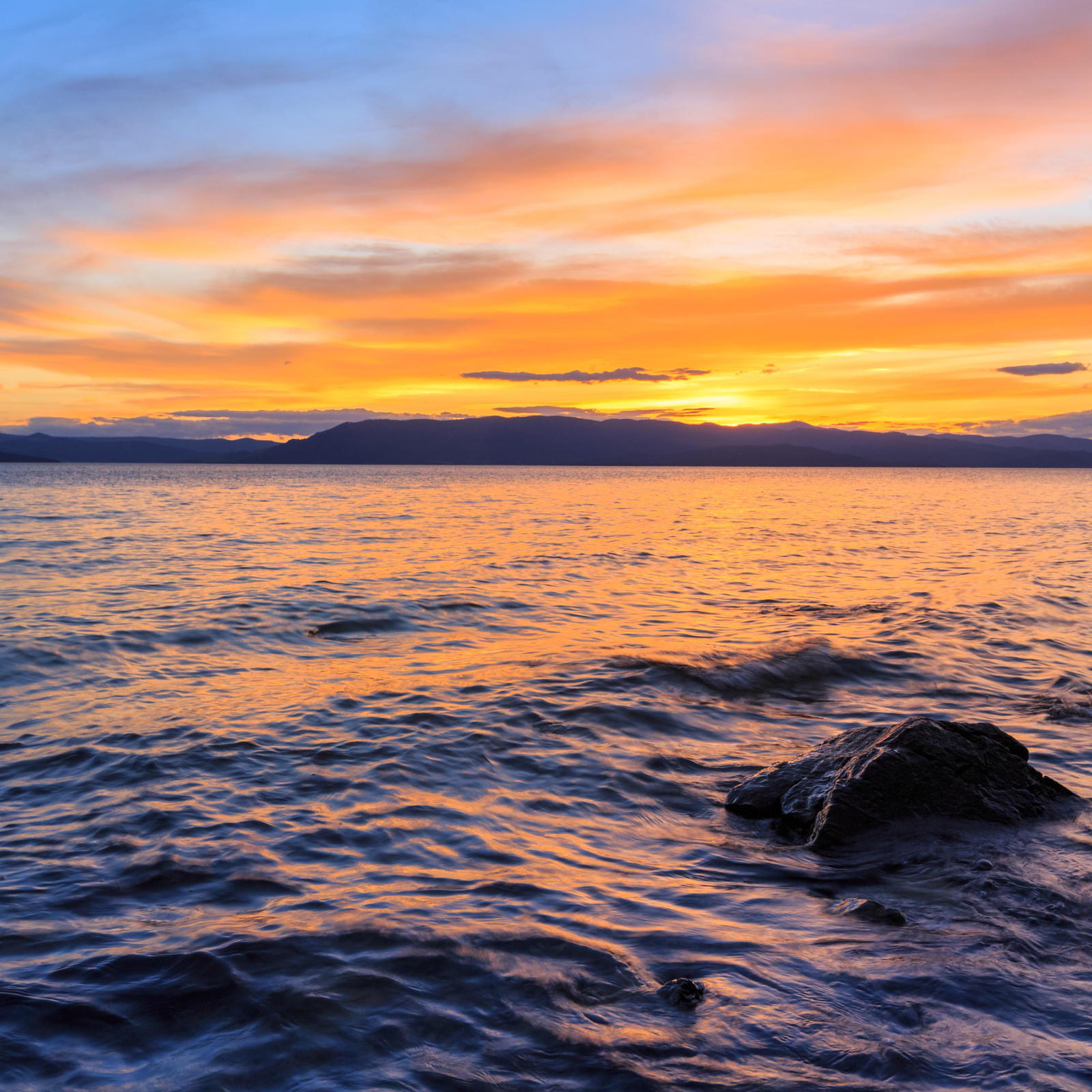 The surface of Flathead Lake shines with yellow and gold colors during sunset