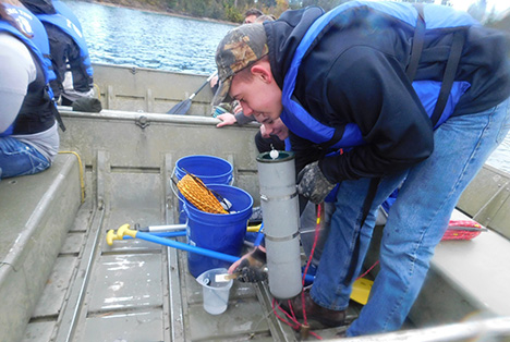 Students prepare to take a water sample from a rowboat