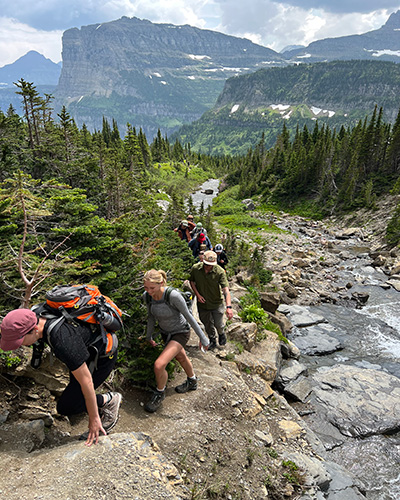 Students hike along Siyeh Creek with the garden face of Heavy Runner Mountain in the background