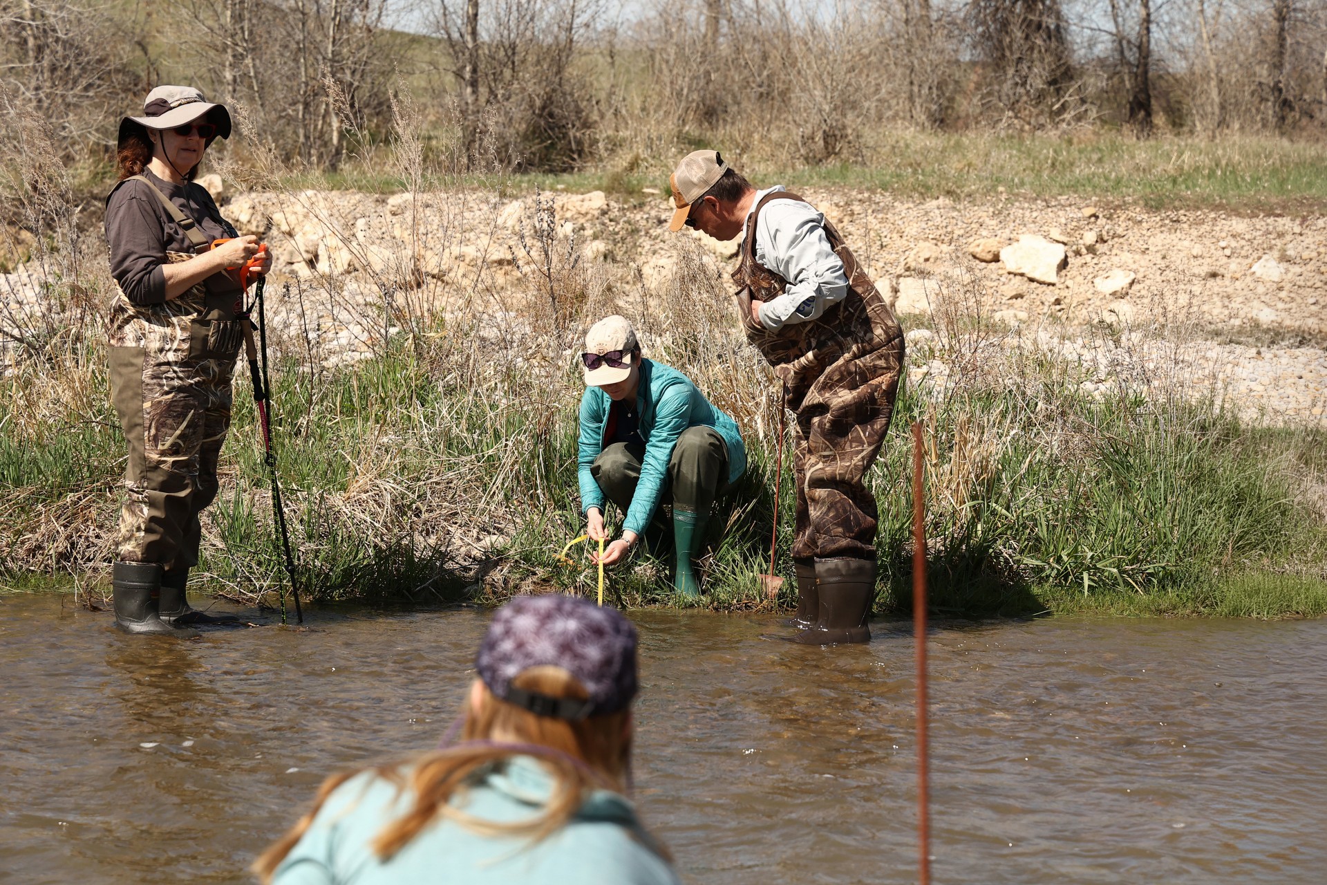 Callie Nelson and Paige Weigand instructing two volunteers on how to measure flow in a stream.