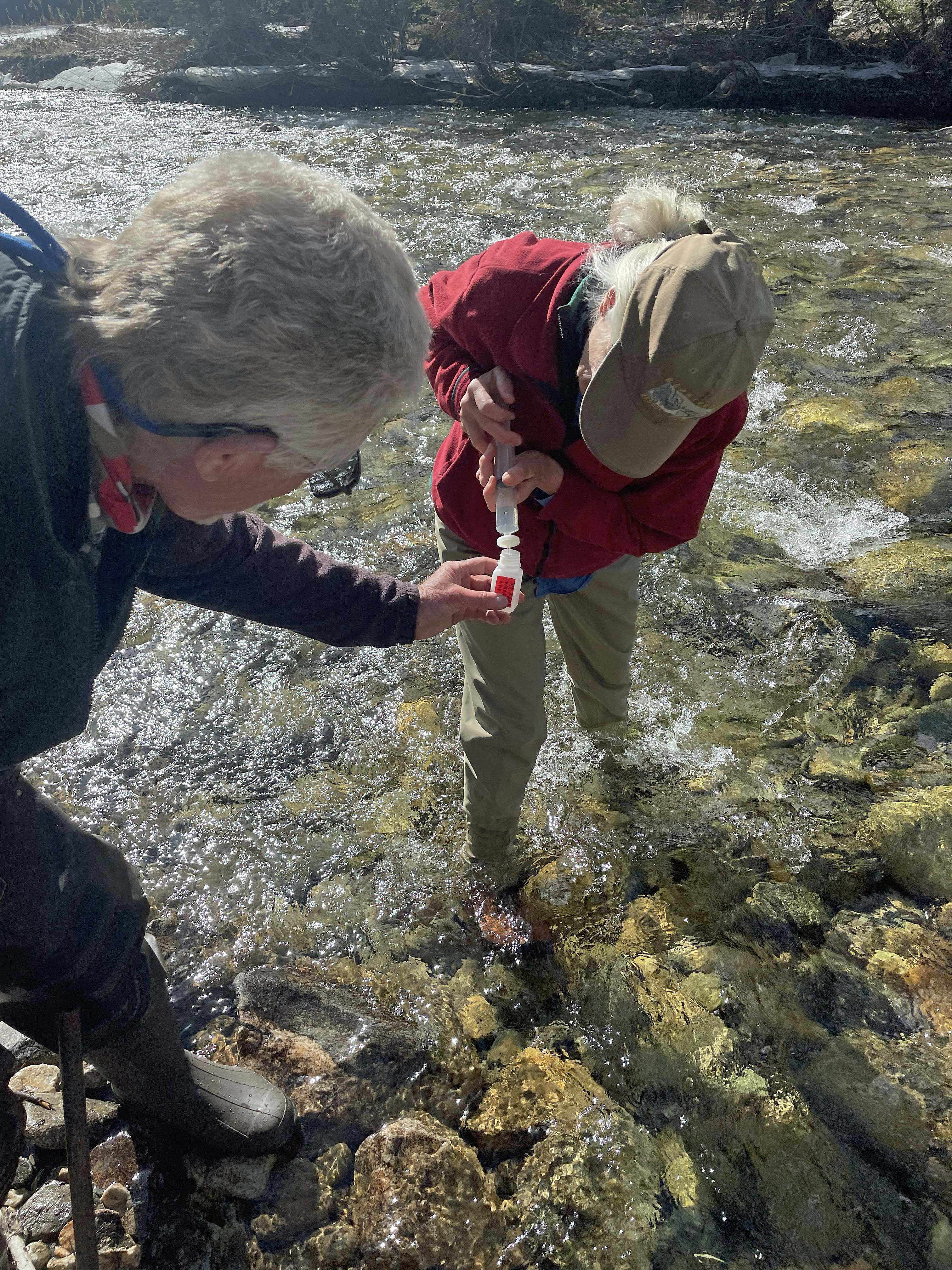 Two Carbon County Resource Council members collecting filtered water sample by pushing water through a filter on the end of a syringe into a small bottle.