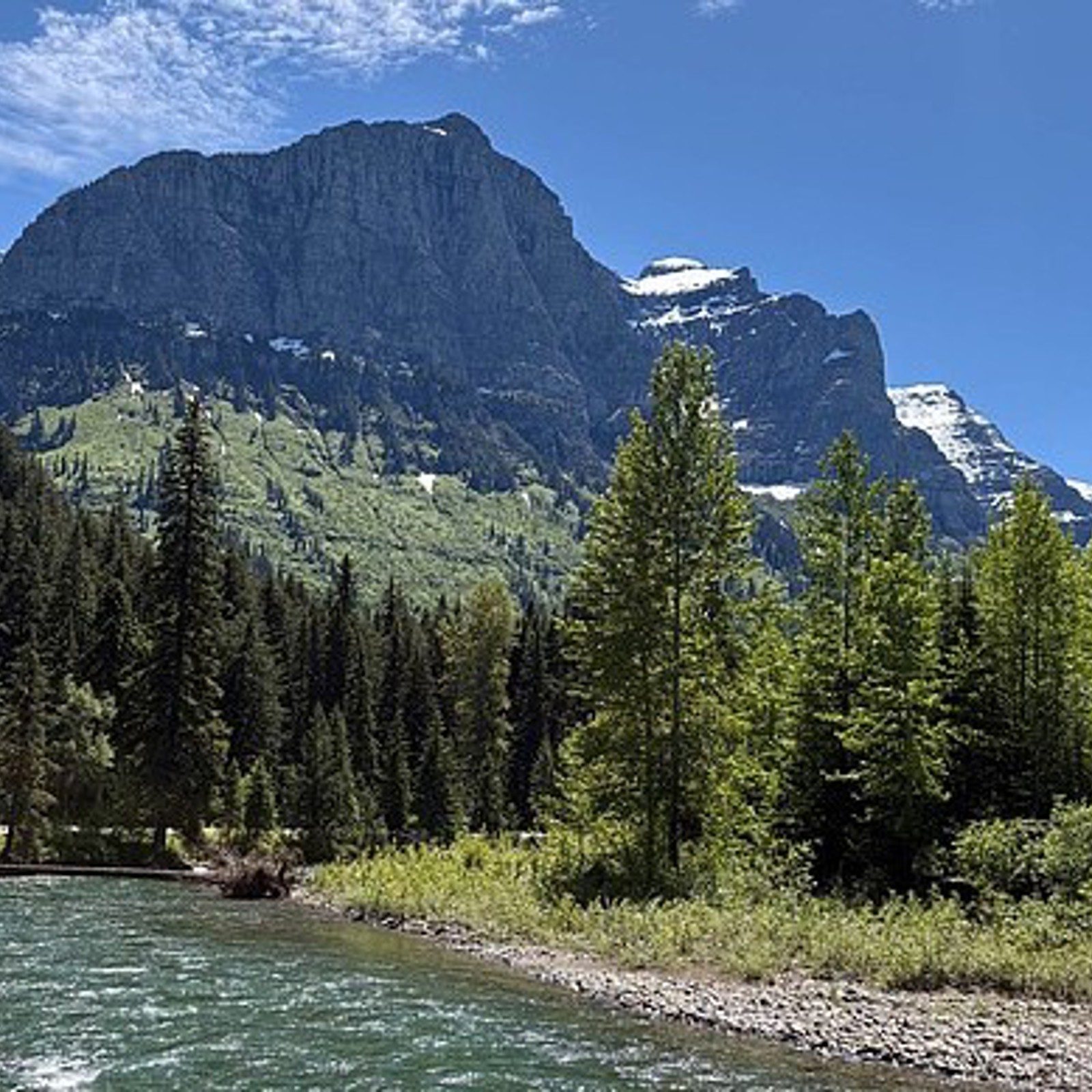 The Middle Fork of the Flathead River flows beneath towering mountains on a sunny summer day.
