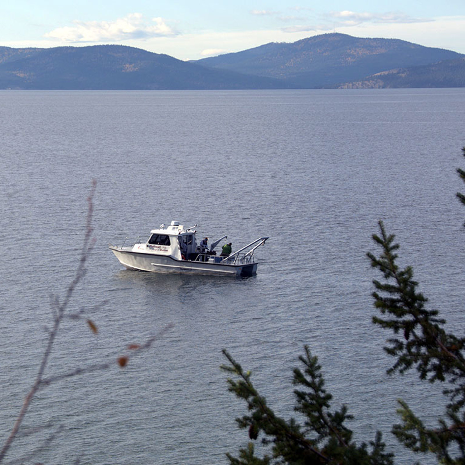 FLBS researchers aboard the Jessie B collect AIS samples off Yellow Bay Point on Flathead Lake with the Salish Mountains in the background 