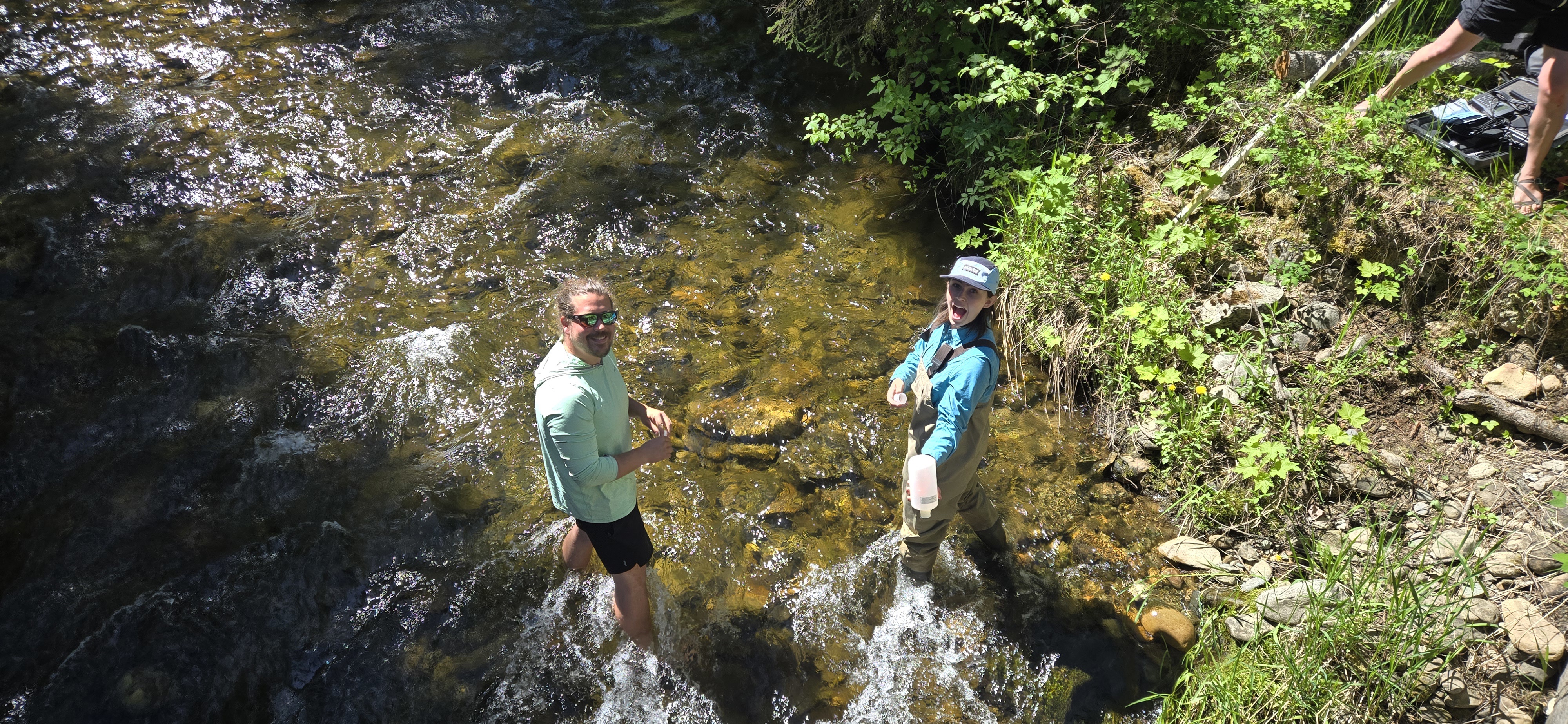 Anthony South and Big Sky Watershed Corp member standing in a river collecting Total Suspended Solids sample in a large bottle.