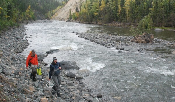 Two researchers standing the the rocky beach of a river in Alaska