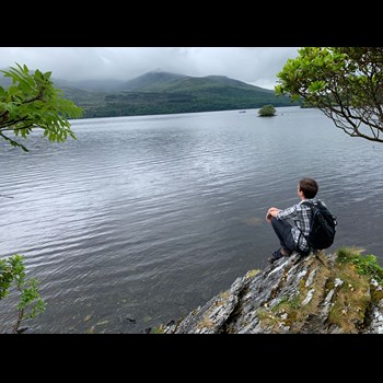 Eliot sitting on a rock overlooking a large body of water with mountains in the background